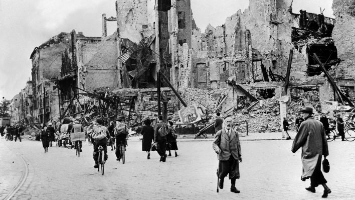 Menschen gehen nach Kriegsende im Mai 1945 auf einer Straße an zerstörten Häusern entlang. (Quelle: dpa-Bildfunk) Menschen gehen nach Kriegsende im Mai 1945 auf einer Straße an zerstörten Häusern entlang. (Quelle: dpa-Bildfunk)