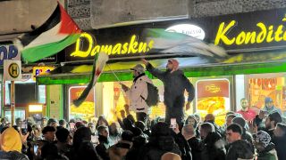 Syrer versammeln sich am Abend des 07.12.2024 im Bezirk Neukölln mit Flaggen vor der Bäckerei Damaskus und feiern den Vormarsch der Rebellen auf Damaskus (Quelle: dpa / Julius-Christian Schreiner).