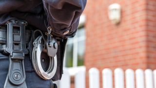 Ein Polizist steht am 21.05.2025 vor einem durchsuchten Haus in Altdöbern. (Quelle: dpa/Frank Hammerschmidt)