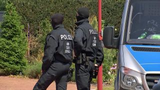 Zwei Polizisten stehen an einem Polizeiauto vor dem Haus in Altdöbern, das durchsucht wird (Foto: rbb/Screenshot)
